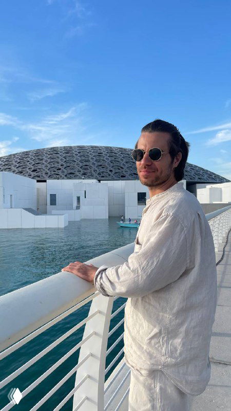 Мужчина в белой рубашке и очках на набережной у современного здания; фото к материалу про таргетинг и копирайтинг.