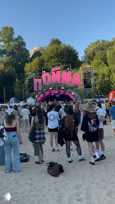 Входная зона фестиваля «Пойма»: большая розовая арка с надписью «Пойма», толпа молодых людей на песчаной площадке и летняя атмосфера перед выступлениями.