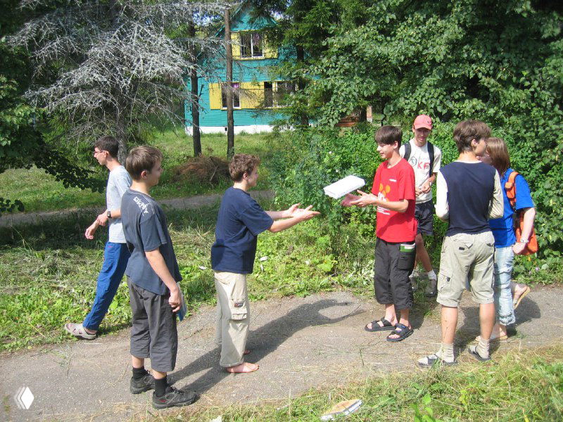 Группа молодых людей на летней площадке передаёт книгу друг другу; сцена напоминает атмосферу ЛКШ и олимпиадных встреч.