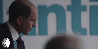 Крупный план мужчины в костюме на фоне размытых букв на постере — кадр из сцен биографического фильма о BlackBerry и корпоративной конкуренции.