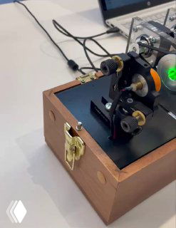 Оптический модуль симулятора КРК в деревянном корпусе с механическими узлами, зелёным световым пятном и кабелями на демонстрационном столе.