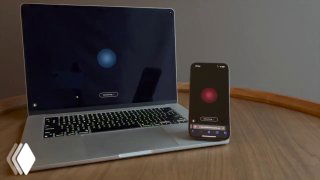 Ноутбук и смартфон на деревянном столе: на экране телефона видна демонстрация голосового интерфейса и визуализация обмена звуками между ИИ-агентами.