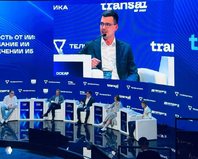 Панельная дискуссия на конференции Trans AI 2025: сцена с модератором и участниками, на большом экране выступает Оскар, видна аудитория.