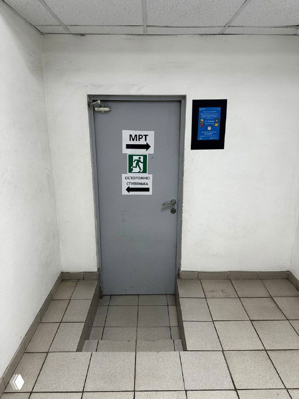 Серая дверь в белом коридоре клиники с наклейками и указателями — пример неинтуитивной визуальной коммуникации.