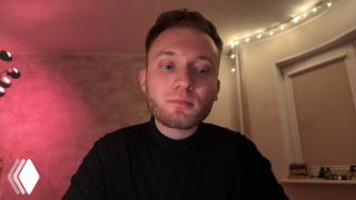 Ведущий в домашней студии смотрит в камеру на фоне тёплой подсветки и книжной полки; кадр из видеорука по визуализации данных.