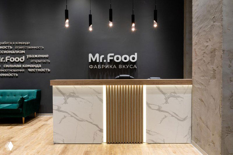 Ресепшн компании Mr.Food: стойка с логотипом «Mr.Food» на фирменном фоне в современном интерьере офисного пространства фабрики.