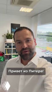 Селфи мужчины в офисном кабинете у окна, на фоне полок с папками и растений; внизу видна надпись «Привет из Питера!» — деловой контекст и рабочая среда.