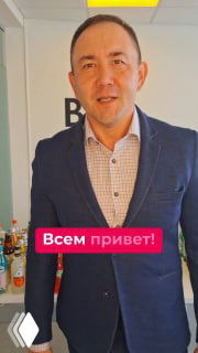 Мужчина в тёмно‑синем костюме на светлом фоне, рядом стол с напитками; видна наклейка «Всем привет!», промо‑кадр для конференции.