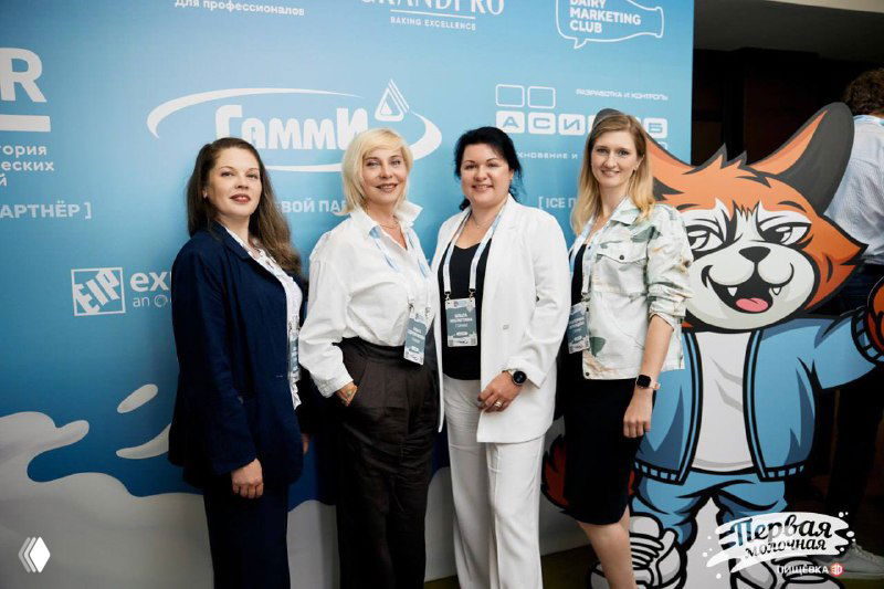 Четыре женщины в деловой одежде на фоне бренд-стены «Гамми» и логотипов конференции, официальная фотография с отраслевого мероприятия в деловой обстановке.