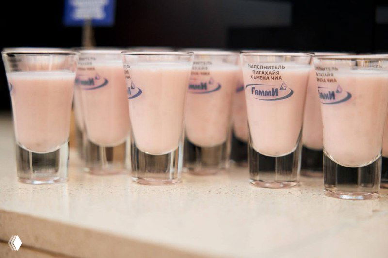 Ряд русских дегустационных стопок с образцами напитков или наполнителей «Гамми», крупный план ингредиентных проб под брендом компании на демонстрации.