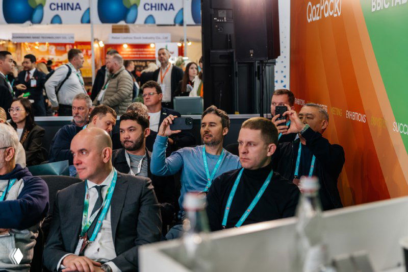 Аудитория и посетители бизнес-сессии: люди слушают доклады, кто-то фиксирует кадры на телефон, видны бейджи участников и деловой контекст.