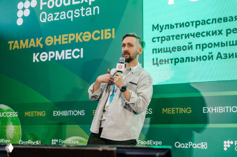 Спикер на зелёной сцене FoodExpo Qazaqstan с микрофоном рассказывает о стратегиях для пищевой промышленности Центральной Азии.
