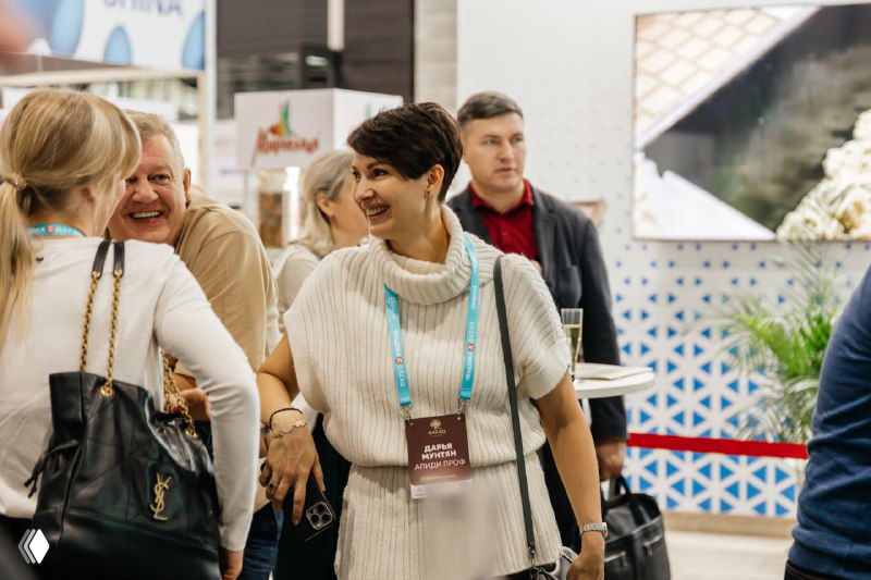 Улыбчивые участники и организаторы на проходе между стендами, люди общаются, изучают экспоненты и обмениваются контактами.