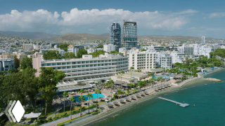 Aerial coastal view of a Cypriot seaside resort with hotels, pools and promenade, illustrating the island life and seaside setting shown in the documentary.