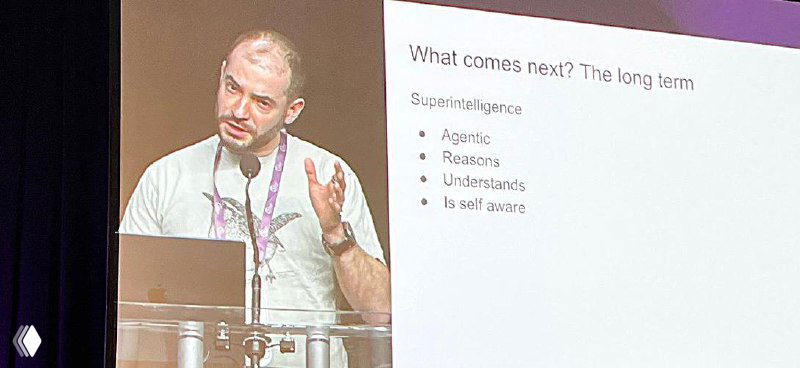 Ilya Sutskever speaking at a conference, at a lectern; projected slide reads 'What comes next? The long term' with bullet points about agentic reasoning