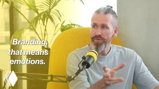 Bearded man speaking into a podcast microphone, seated in a yellow chair in studio with plants; on-screen text about branding.