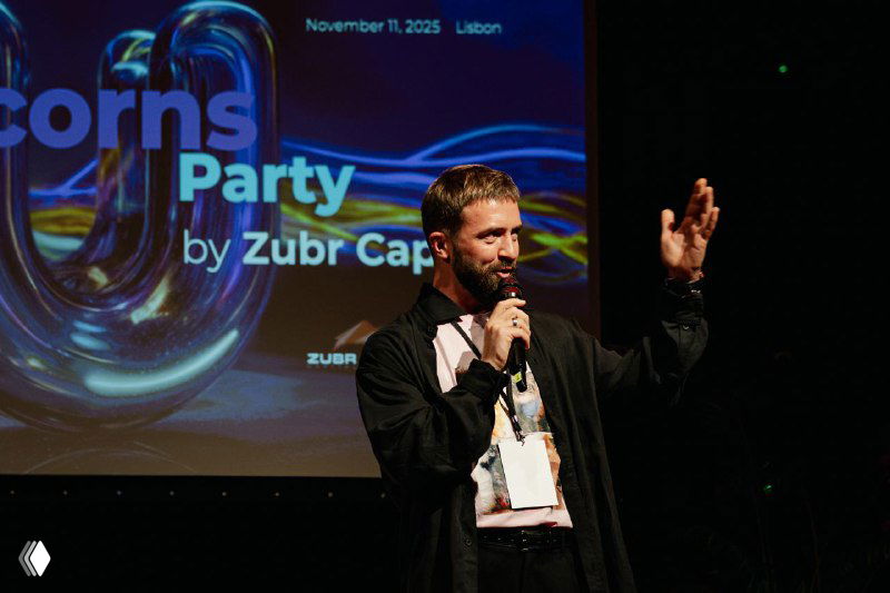 Speaker on stage holding a microphone during the Future Unicorns Party 2025 in Lisbon, branded backdrop showing event title and sponsor logos.
