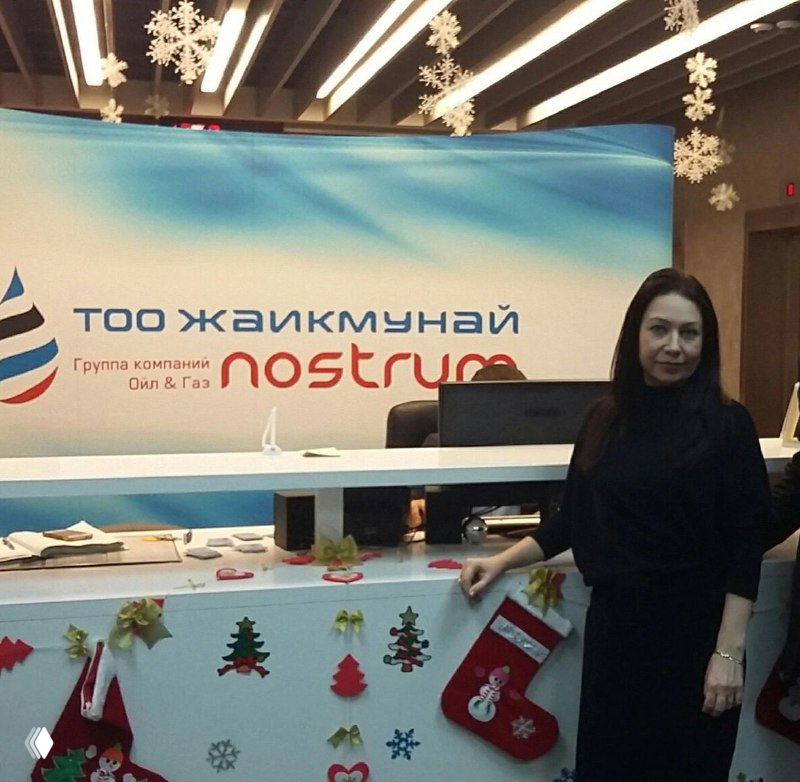 Женщина у стойки регистрации на фоне баннера с логотипом «КазМунайГаз / nostrum», фото с рабочей поездки и переговоров.