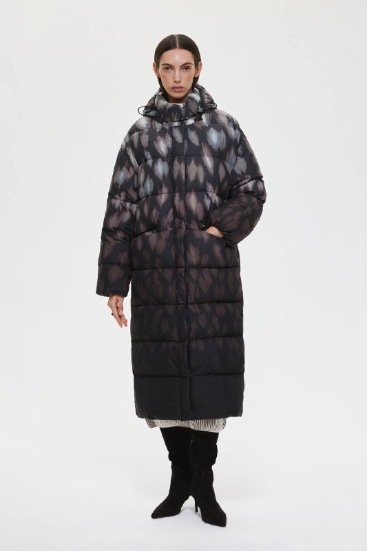Длинный стёганый пуховик тёмных тонов на модели, высокий воротник и свободный крой для комфортного зимнего образа в капсуле.