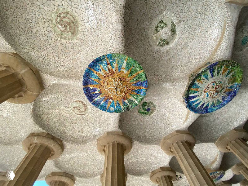 Мозаичный потолок с яркими круглыми вставками и рядом колонн — интерьер с характерной испанской архитектурной отделкой, вид снизу.