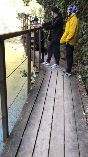 Деревянный настил с перилами в ущелье; трое людей в тёплой одежде стоят у ограждения и наблюдают реку.