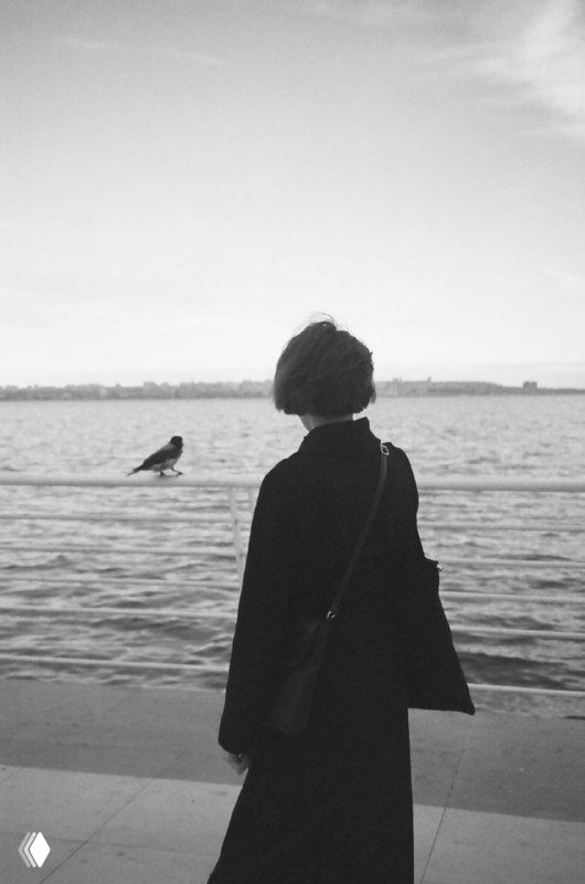 Чёрно‑белая фотография: силуэт человека у реки, птица на парапете и тихий берег — образ спокойствия и возвращения в настоящее.
