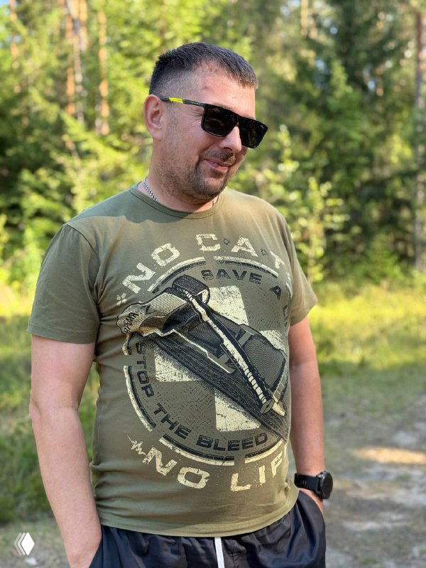 Мужчина в солнцезащитных очках и футболке стоит в лесу на летней тропе; фотография декоративная, не связана напрямую с текстом.