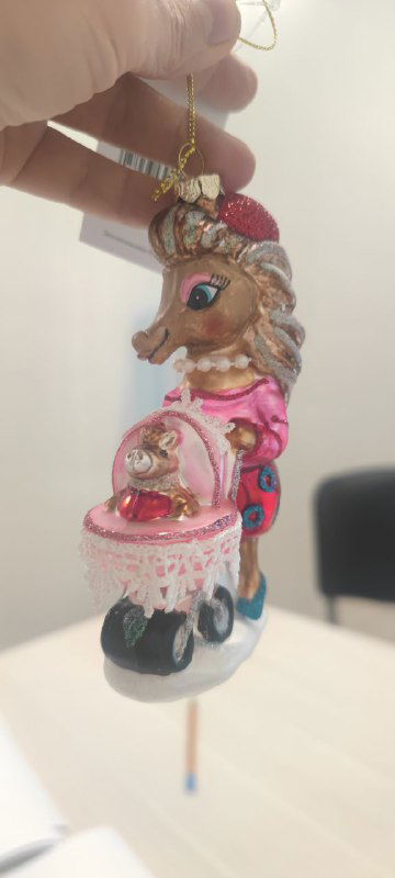 Крупный план бокового ракурса той же игрушки‑лошадки: акцент на розовой и золотой росписи, миникарете и мелких декоративных элементах изделия.