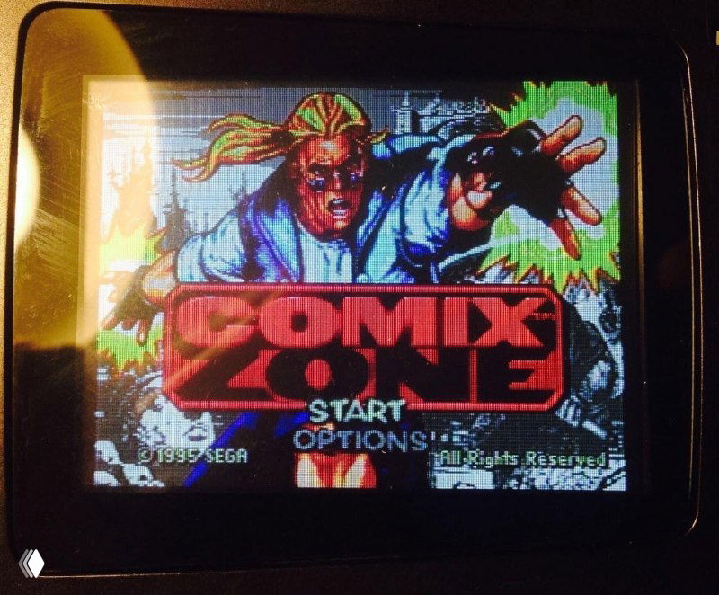 Крупный план модифицированного экрана SEGA Nomad, отображающего заставку игры Comix Zone с насыщенными цветами и чёткой пиксельной графикой на включённом дисплее.