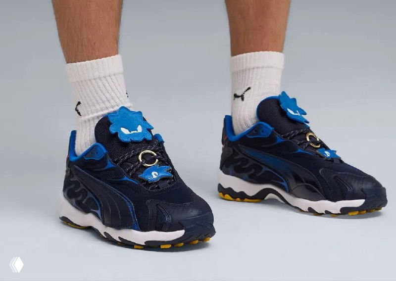 Синие кроссовки Puma из коллаборации Sonic Racing на ногах модели с белыми носками и логотипом Puma — вид в профиль, подчёркивающий дизайн подошвы.