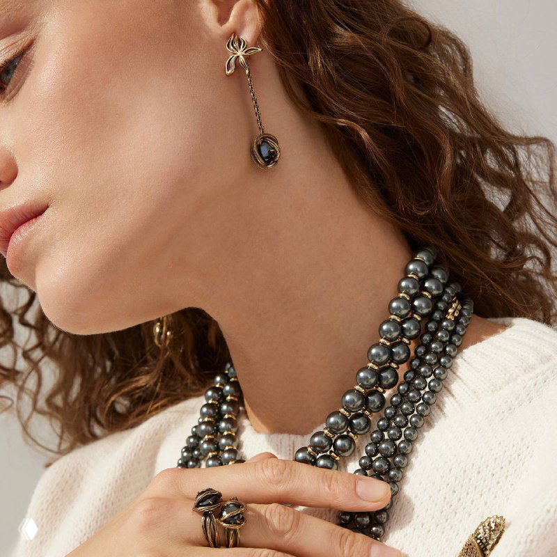 Модель в профиль носит серьгу‑компаньон Fiore di Firenze: образ в нейтральной одежде и многорядное жемчужное украшение на шее.