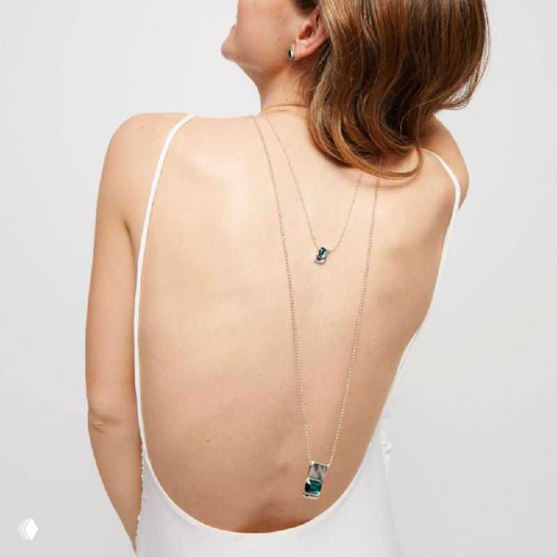 Вид спины модели в платье с открытой спиной, на которой висят два длинных подвеса с зелёными кристаллами из коллекции Ser Magnetica.