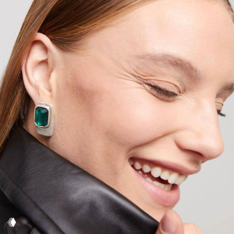 Крупный план профиля улыбающейся модели в серьгах с зелёными камнями — демонстрация посадки и дизайна украшения.