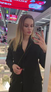 Фотография продавца/модели в зеркале в магазине — женщина в чёрном пиджаке делает селфи на фоне витрин с украшениями, интерьер ТЦ виден за спиной.