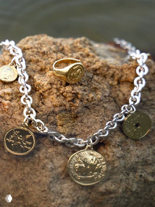 Крупный план цепочки с монетами и перстнем на текстурированном фоне, показана фактура и металлы коллекции Kubik/France от CICLON