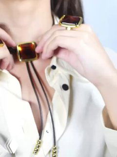 Кадр из видео: руки держат bolo-ожерелье с квадратной вставкой, демонстрируется посадка украшения на шее и детализация застёжки