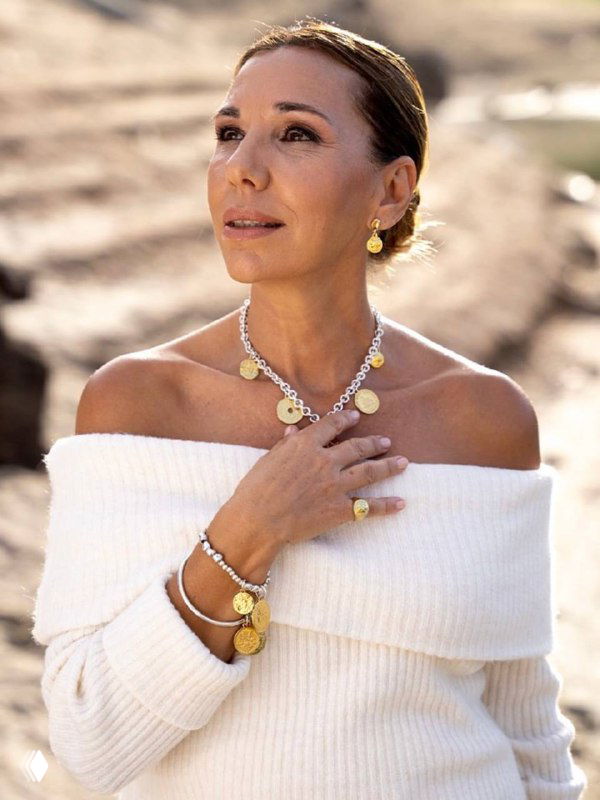 Женщина в лёгком белом топе на природе демонстрирует колье и браслеты из золотой линии коллекции CICLON, естественный свет подчёркивает металл