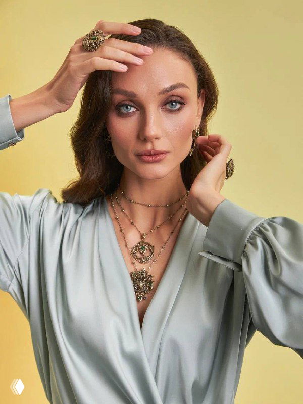 Портрет модели в светлом платье, на котором видны несколько слоёв ожерелий и брошь‑подвеска из линии «Маска‑Природа», показ сочетания украшений.