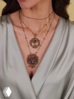 Детальный крупный план декольте с двумя подвесками разного размера и фактуры, одна из которых превращается в брошь‑аксессуар, акцент на деталях отделки.