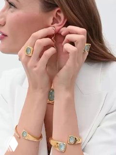 Женщина примеряет серьги и демонстрирует набор украшений с небесно‑пастельными камнями: аккуратный маникюр и светлая одежда, светлый студийный фон.