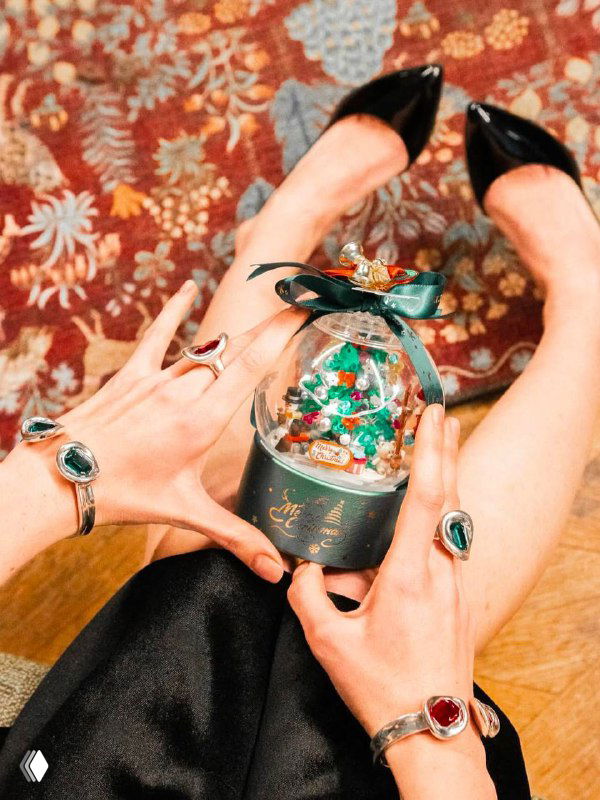 Крупный план рук с кольцами и браслетами, модель держит декоративный праздничный шар в руках, сцена создает новогоднее настроение и акцент на аксессуарах.