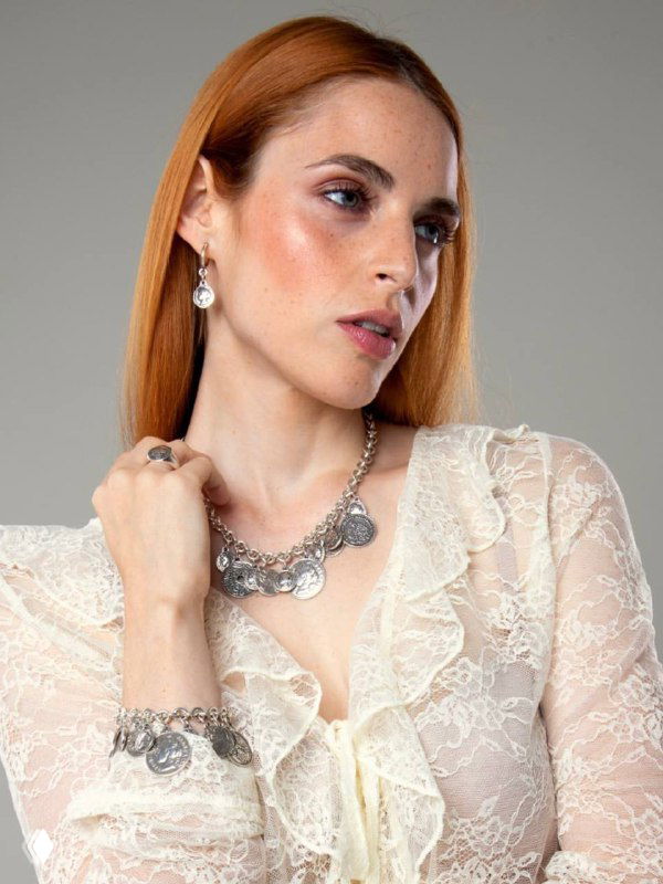 Портрет женщины в светлом образе с ожерельем и серьгами CICLON; акцент на монетных подвесках и классической ювелирной стилистике испанского бренда.