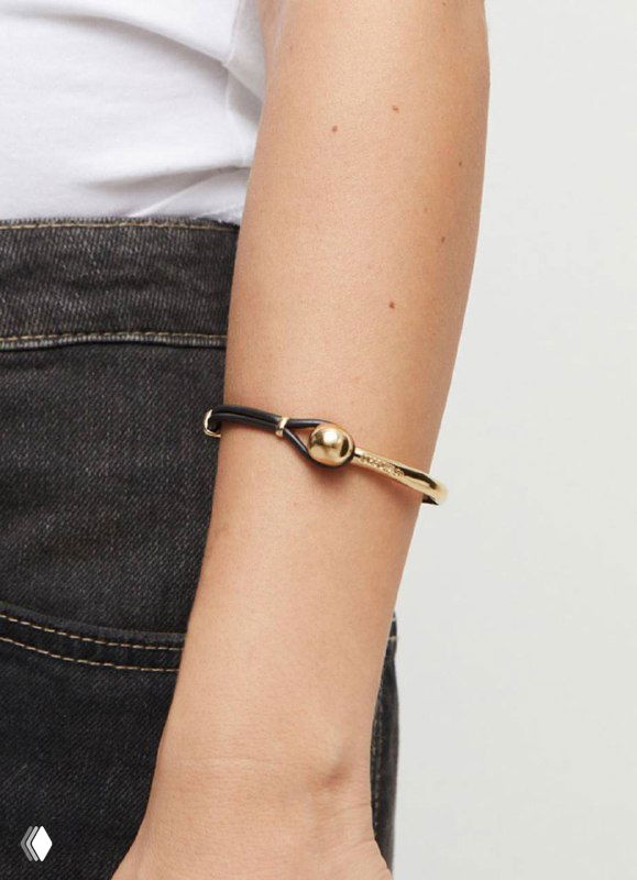 Браслет UNOde50 крупным планом: золотая полусфера и кожаная вставка на запястье на фоне джинсов, рекламная съемка аксессуара.