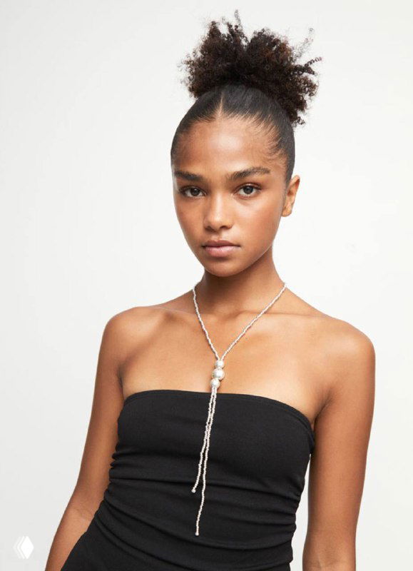 Модель в длинном украшении UNOde50 Ser Intrepida: кулон с полусферами и серебристая отделка, образ на светлом фоне.