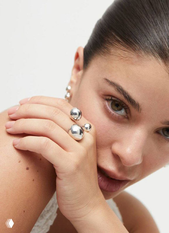 Крупный план кольца и пальцев модели, украшения UNOde50 Ser Intrepida с металлическими полусферами и чистой студийной подачей.