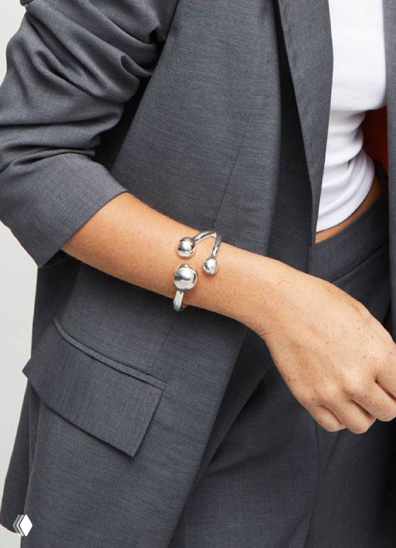 Запястье модели с браслетом UNOde50: сочетание полусфер и кожаной вставки, образ в деловом костюме, рекламный кадр коллекции.