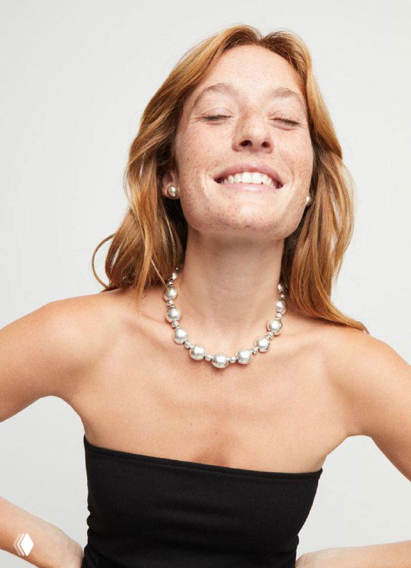 Улыбчивая модель в ожерелье из крупных серебристых полусфер UNOde50 Ser Intrepida на светлом фоне, рекламный образ коллекции.