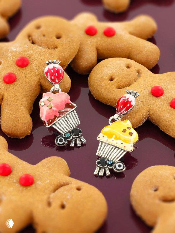 Крупный план ярких эмалевых серьг TARATATA в форме кексов и ягод на тёмном фоне рядом с пряничными фигурками — декоративная презентация коллекции.