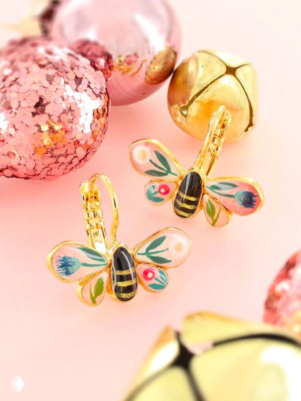 Пара серьг TARATATA в виде ярких эмалевых пчёл с золотистыми элементами на розовом праздничном фоне с блёстками.