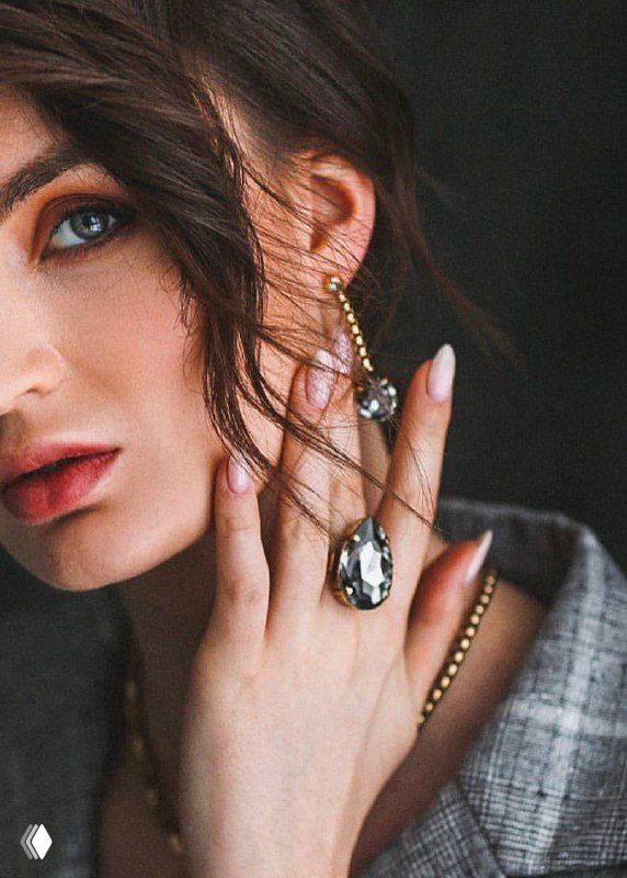 Крупный план модели с висящими серьгами и кольцом Claudio Canzian; акцент на дизайне украшений, рука и текстура одежды создают стильный контекст.